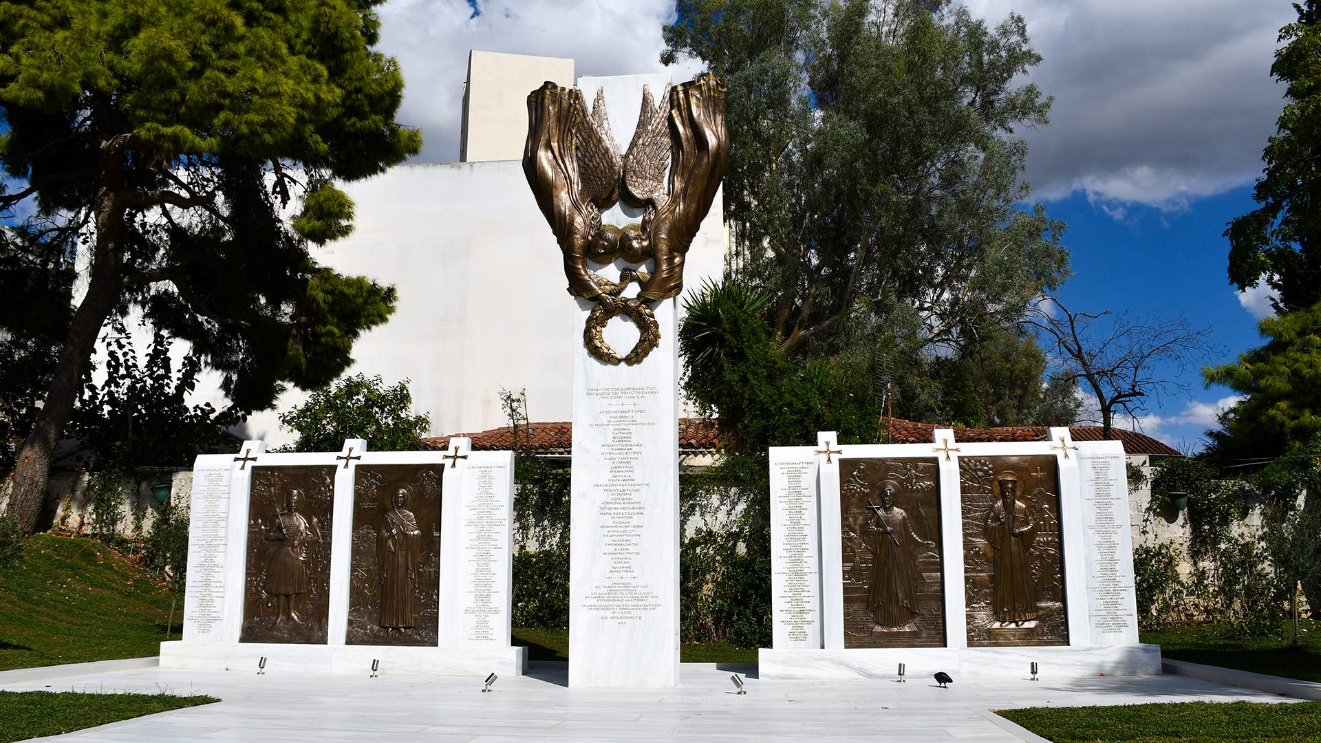 Ένα λευκό μνημείο που βρίσκεται σε μια καταπράσινη περιοχή με πάρκο, με ανάγλυφα από μπρούντζο στην κορυφή του και χαραγμένα ονόματα πάνω του.