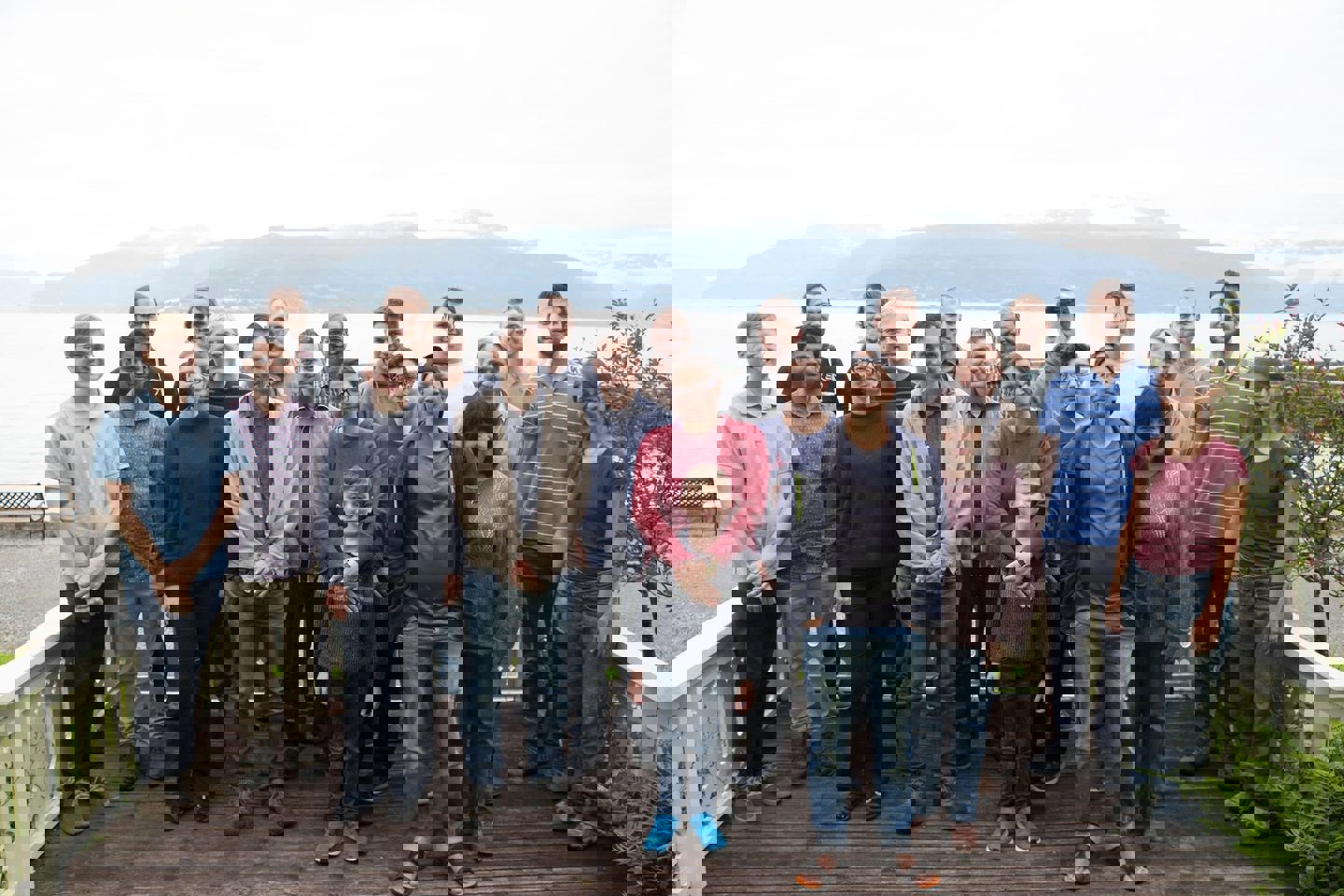 A group of people standing on a wooden deck in front of sea for a photo.
