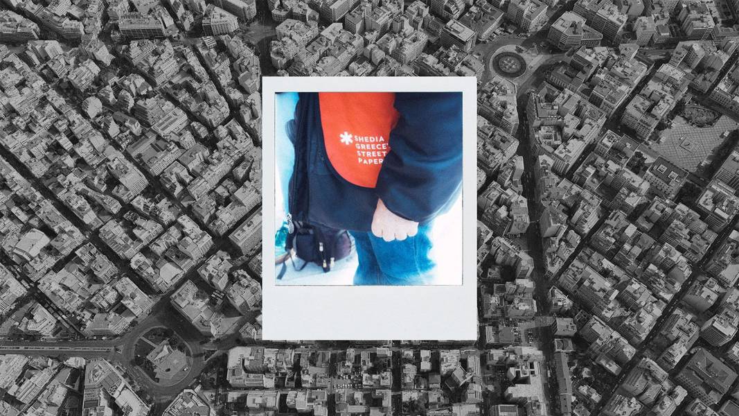 In the center of a black and white aerial photograph of downtown Athens is a colored polaroid showing the lower body of a man in a red vest from the street paper