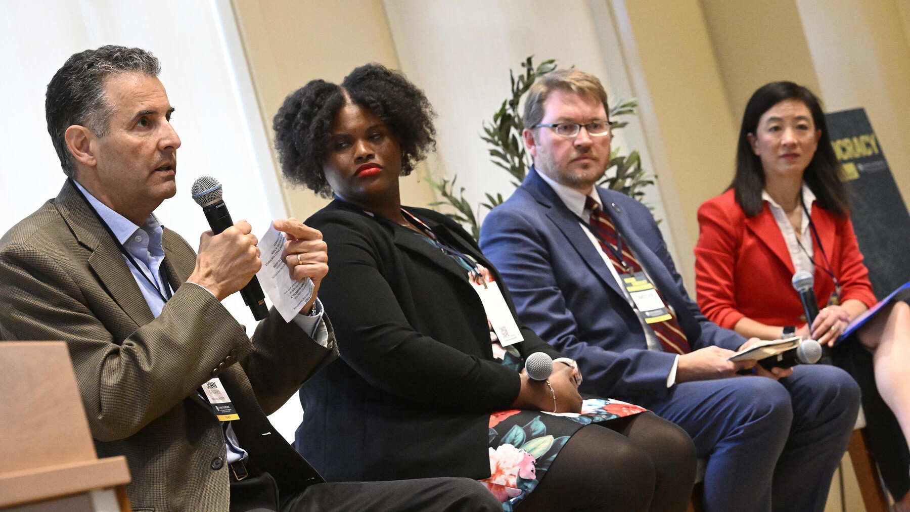 Panelists speak at an SNF Agora Institute discussion, with one man addressing the audience while others listen attentively.